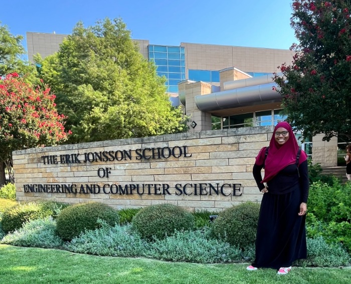 student scholar stands in front of UT-Dallas campus